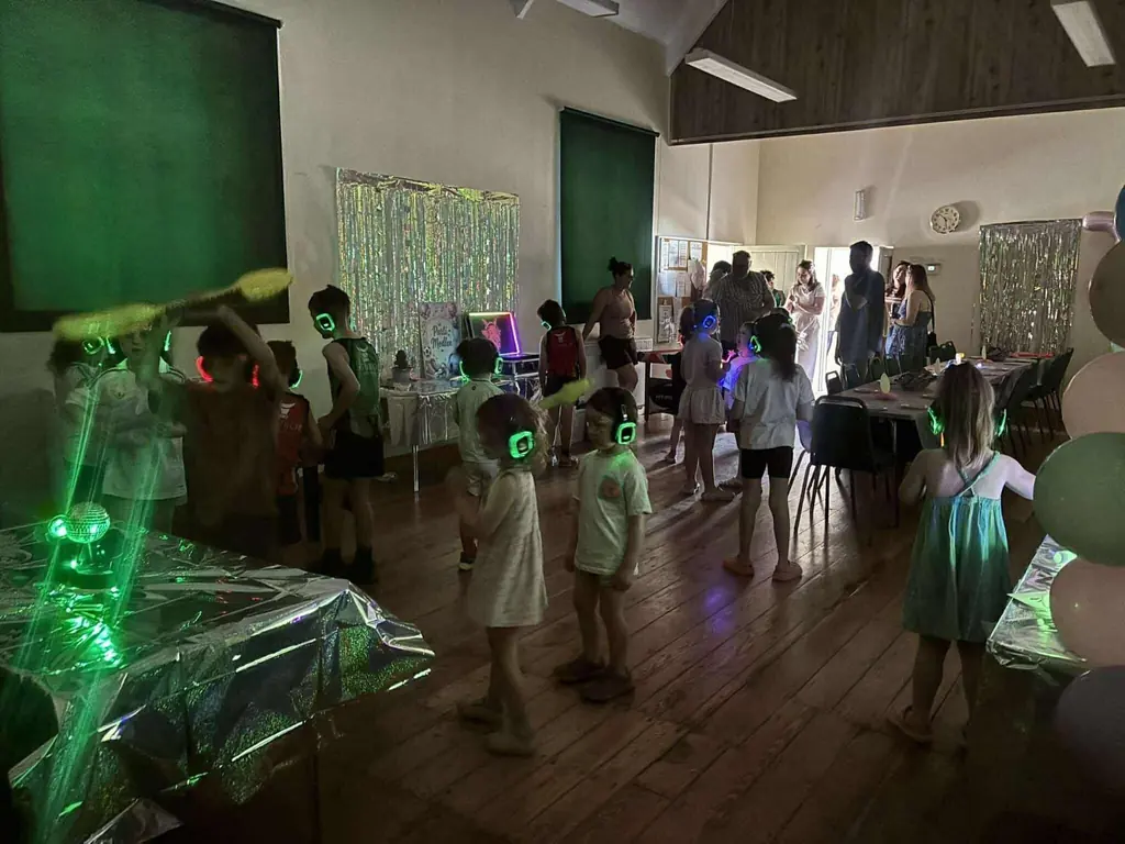 Children in glowing silent disco headphones dancing at a party in a hall.